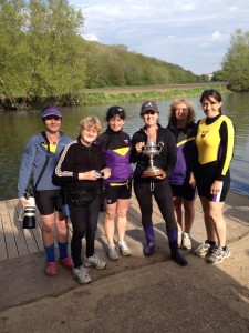 Six ladies stood by a river bank holding a trophy