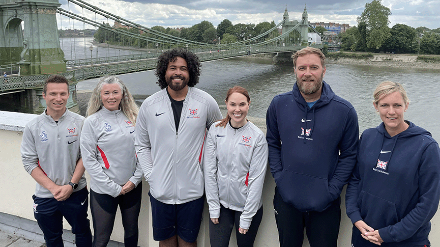 Group in British Rowing tops pictured in front of Hammersmith Bridge