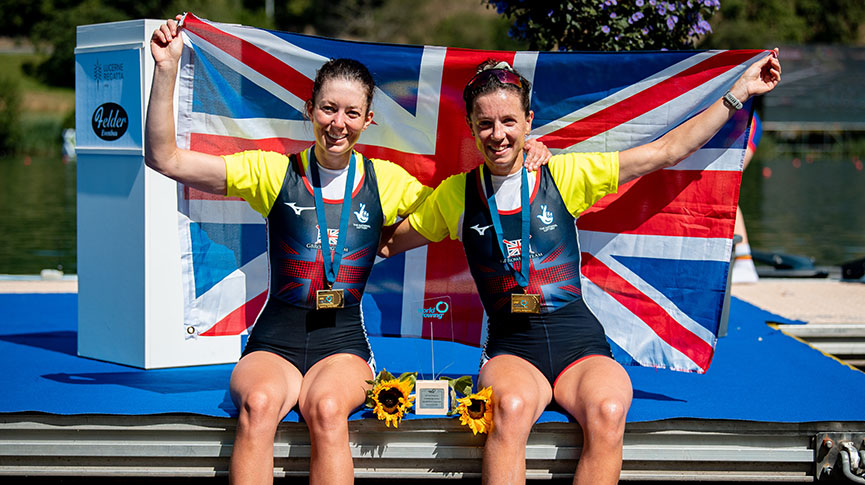 2 women sitting on landing stage with medals and GB flag