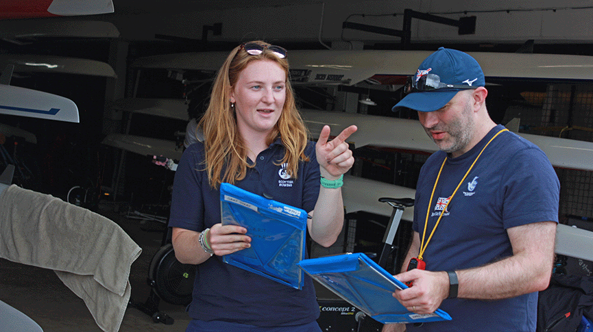 Two coaches with clipboards in the boathouse