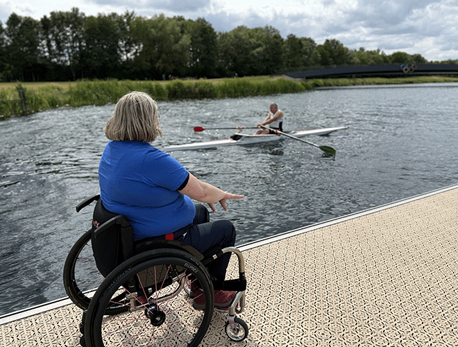 Coach in a wheelchair coaching single sculler from the pontoon