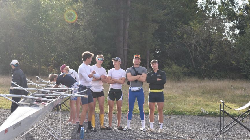 Some male newcastle uni bc rowers smiling at the camera next to a boat