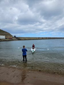 A person coaching a single scull from the beach