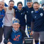 A group of people stood round one person who is sat on a rowing machine