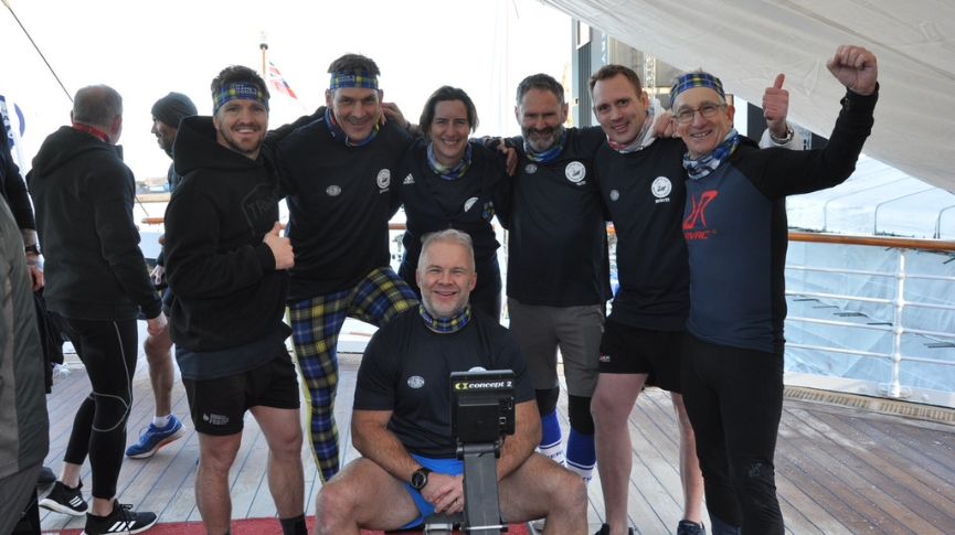 A group of people stood around one person sitting on a rowing machine